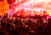 Illegal Rave INVADES Military Site Crowd at concert with vibrant stage lights.