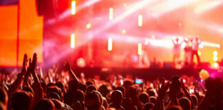 Illegal Rave INVADES Military Site Crowd at concert with vibrant stage lights.