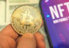 TRUMP’S Crypto Gamble Backfires—$405M Vanishes! Person holding Bitcoin coin, NFT text on screen.