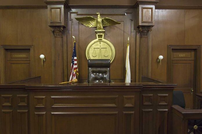 Empty,Courtroom,With,Chair,Of,Judge,And,Flags Interior of a courtroom featuring a judges bench and American flag