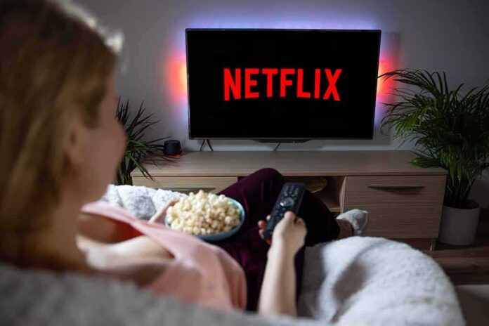 Person watching Netflix on TV with popcorn and remote