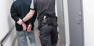 New Video Sharpens About The Case Officer escorting handcuffed person down hallway.