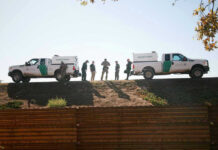 Drug Busts at the Border Put Cartel Fight Border Patrol vehicles and agents on a ridge.