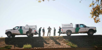 Drug Busts at the Border Put Cartel Fight Border Patrol vehicles and agents on a ridge.