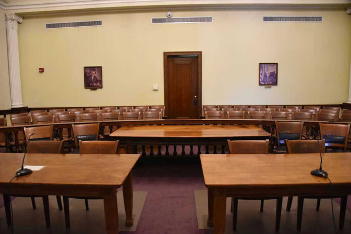 1291095706-1 Empty courtroom with wooden tables, chairs, and a door.