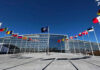 Eastern Europe Seeks Stronger Nuclear Deterrence Flags outside NATO headquarters building under clear blue sky.
