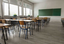 Predator Hunted Kids In Plain Sight Empty classroom with desks, chairs, windows, and chalkboard.