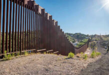 Border Wall Expansion Triggers Property Rights Clash in West Texas Tall metal border wall with rural landscape.