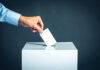 Hand placing ballot into voting box.