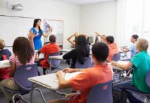 Classroom Power Flip Stuns America Teacher in a blue dress instructing students in a classroom with hands raised