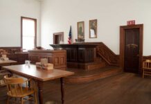 Bolton Busted: Top Secret Chaos Interior of a historic courtroom with wooden furniture and an American flag