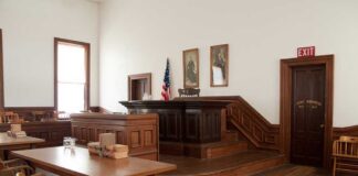 Bolton Busted: Top Secret Chaos Interior of a historic courtroom with wooden furniture and an American flag