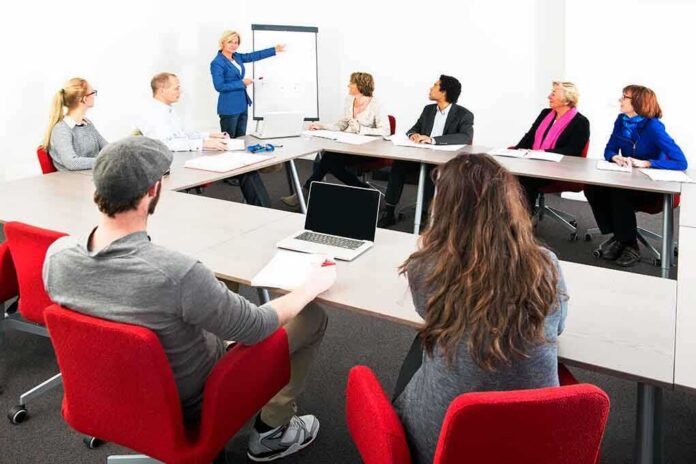 shutterstock_158984081 A diverse group of professionals engaged in a meeting with a presenter at a whiteboard
