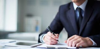 Justice Department’s Leak Investigation Sparks Debate A man in a suit writing notes at a desk with documents and a tablet
