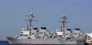 Warplanes Fly, Diplomacy Waits Three gray naval destroyers docked side by side at a pier