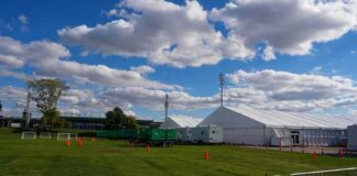 Temporary white tents and equipment on a grassy field with traffic cones and metal barriers