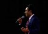 Viral Patriotism Message Sparks National Debate Man in a suit speaking into a microphone on stage
