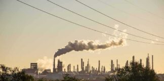 Industrial refinery with smokestack emitting plume at sunset