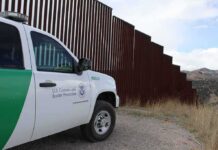 Border patrol SUV parked beside tall steel border fence