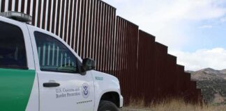 Border patrol SUV parked beside tall steel border fence