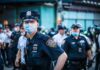 Bass Calls for Answers After Deadly Videos Police officer in mask among colleagues at a city street gathering