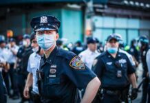 Bass Calls for Answers After Deadly Videos Police officer in mask among colleagues at a city street gathering