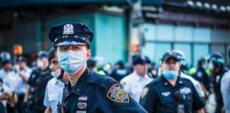 Bass Calls for Answers After Deadly Videos Police officer in mask among colleagues at a city street gathering
