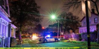 Police car blocks residential street at night behind caution tape