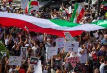 Iranian Leadership Urges Regional Unity Against US and Israel Crowd of protesters holding signs and a large tricolor flag