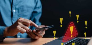Person using smartphone near laptop with warning icons