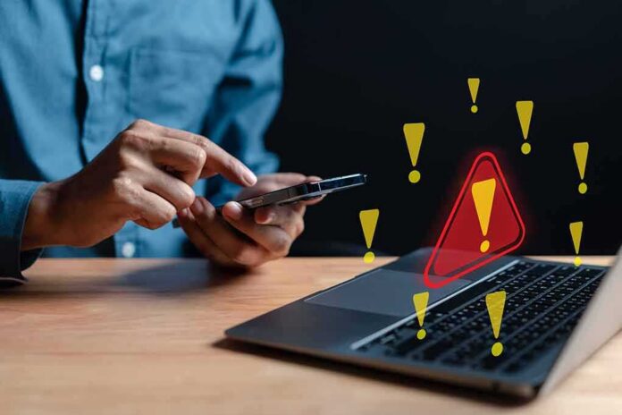 shutterstock_2233922127 Person using smartphone near laptop with warning icons