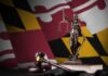Maryland’s Big Tech Tax Collapses Lady Justice statue with gavel and book before a colorful flag backdrop