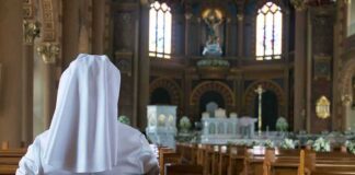 Person in white habit seated in a church pew facing the altar