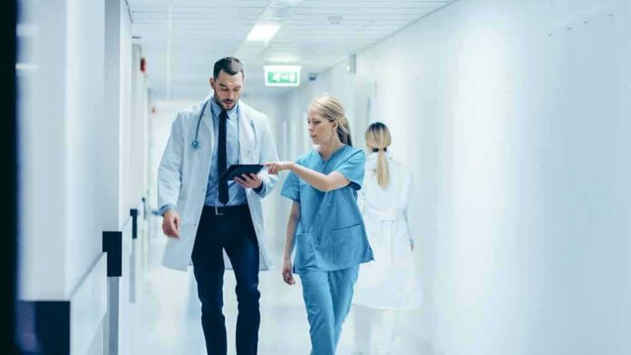 shutterstock_1189798168 Doctor and nurse walking in a hospital corridor reviewing a tablet