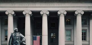 Statue in front of a neoclassical government building with columns and a U.S. flag