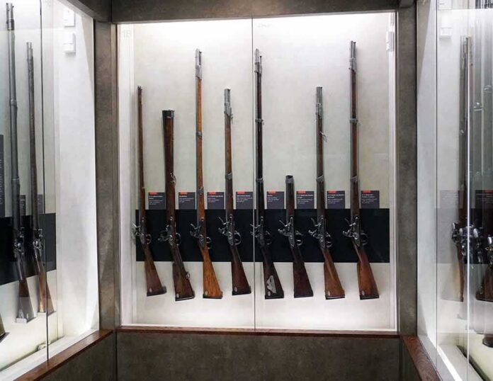 shutterstock_1351647503 Display case with a row of antique muskets