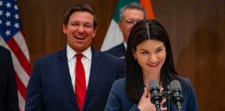 Florida House Race Draws TV Controversy Ron DeSantis smiling behind a woman speaking at a podium