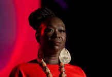Joy-Ann Reid on stage in dramatic lighting wearing a red outfit and large earrings