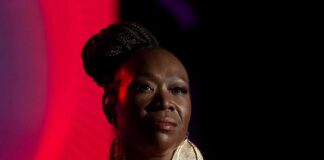 Joy-Ann Reid on stage in dramatic lighting wearing a red outfit and large earrings