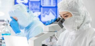 Scientist in protective suit using a microscope