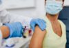 Healthcare worker gives vaccine injection to masked patient