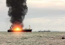 Cargo ship on fire with thick black smoke at sea