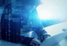 Hooded figure using a laptop with digital code overlay