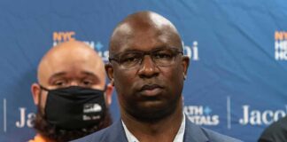 Man in suit and glasses at a press conference