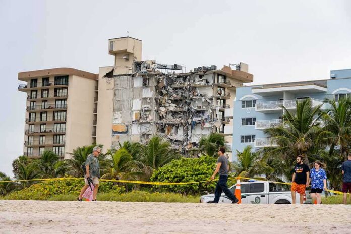 shutterstock_1996561037 Partially collapsed beachfront apartment building behind people walking on sand