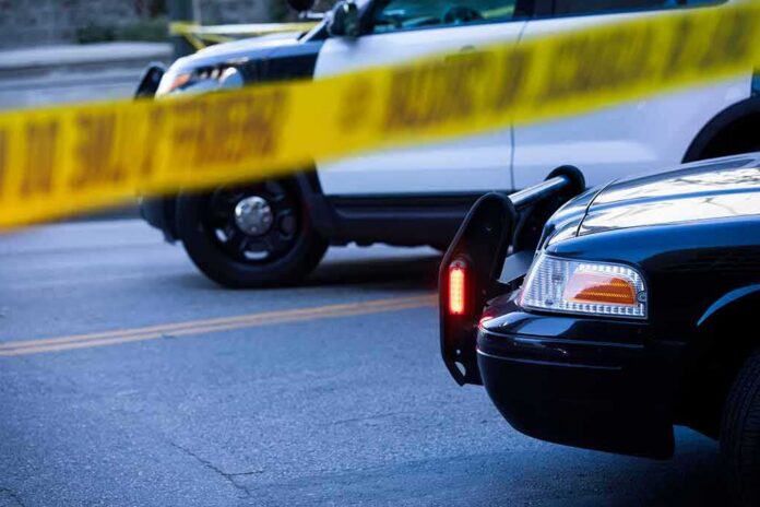 shutterstock_2097855037 Police cars behind yellow caution tape at a street scene