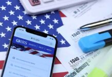 Smartphone showing IRS website on top of tax forms and office supplies