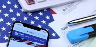 $3M Online Income, Unpaid Taxes Smartphone showing IRS website on top of tax forms and office supplies
