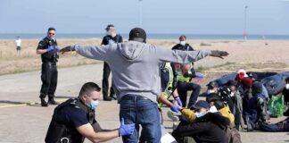 Police officers process group of people on a beachside pavement