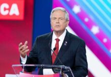 Five-Part Plan Outlined for Republican Midterm Strategy Man in suit speaking at a podium on a colorful stage